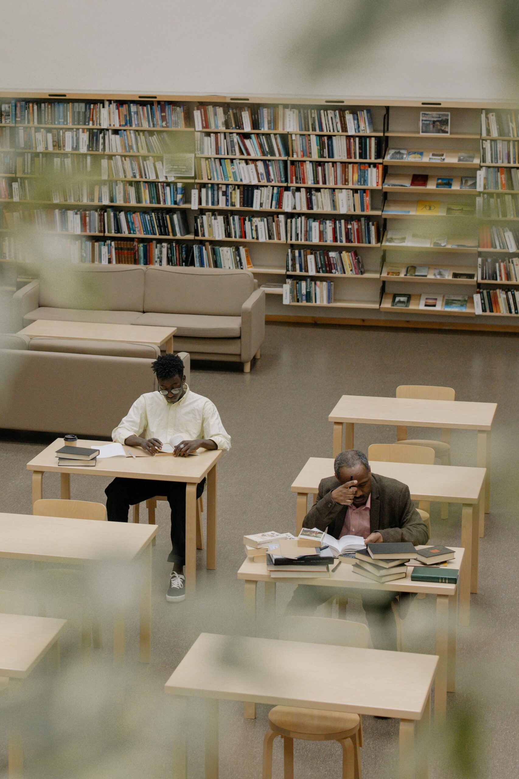 Two men engrossed in reading inside a peaceful library with wooden furniture.